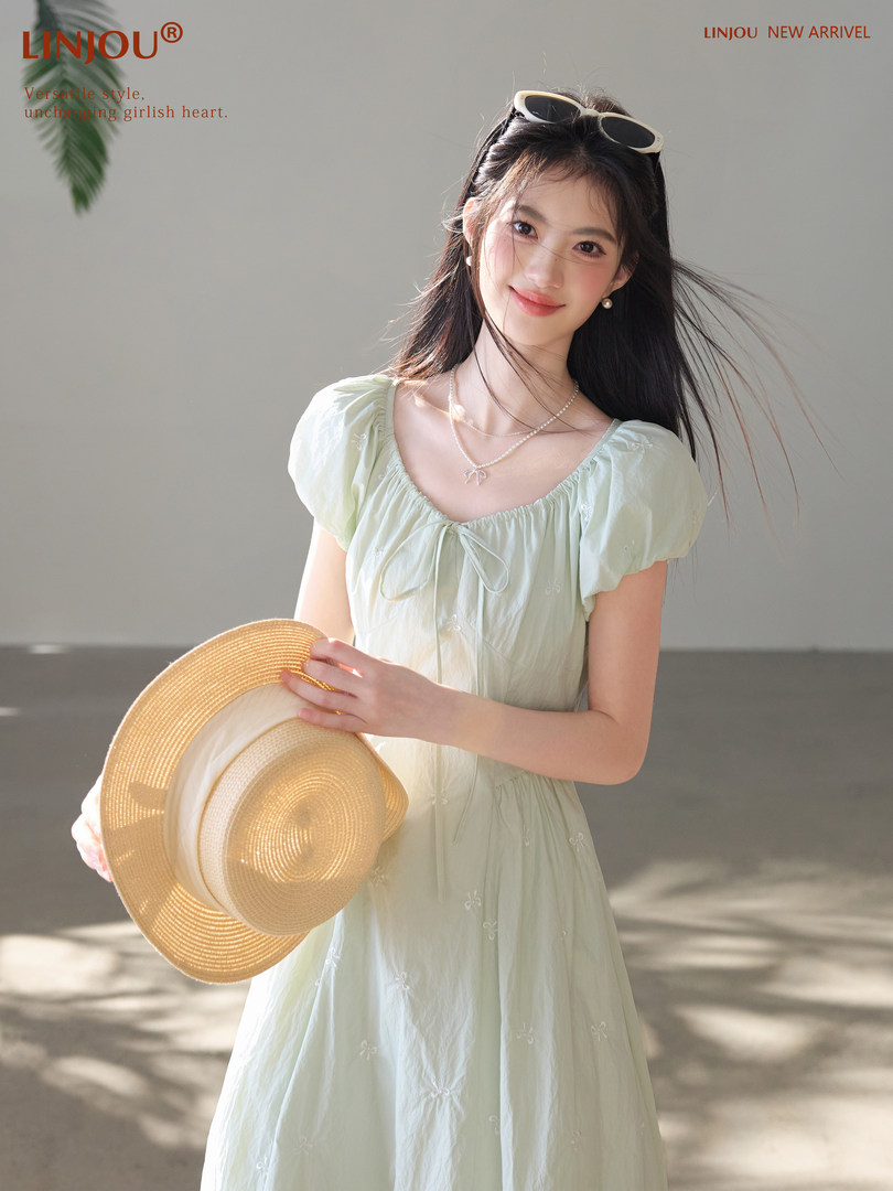 Model wearing a light mint puff-sleeve dress and holding a straw hat