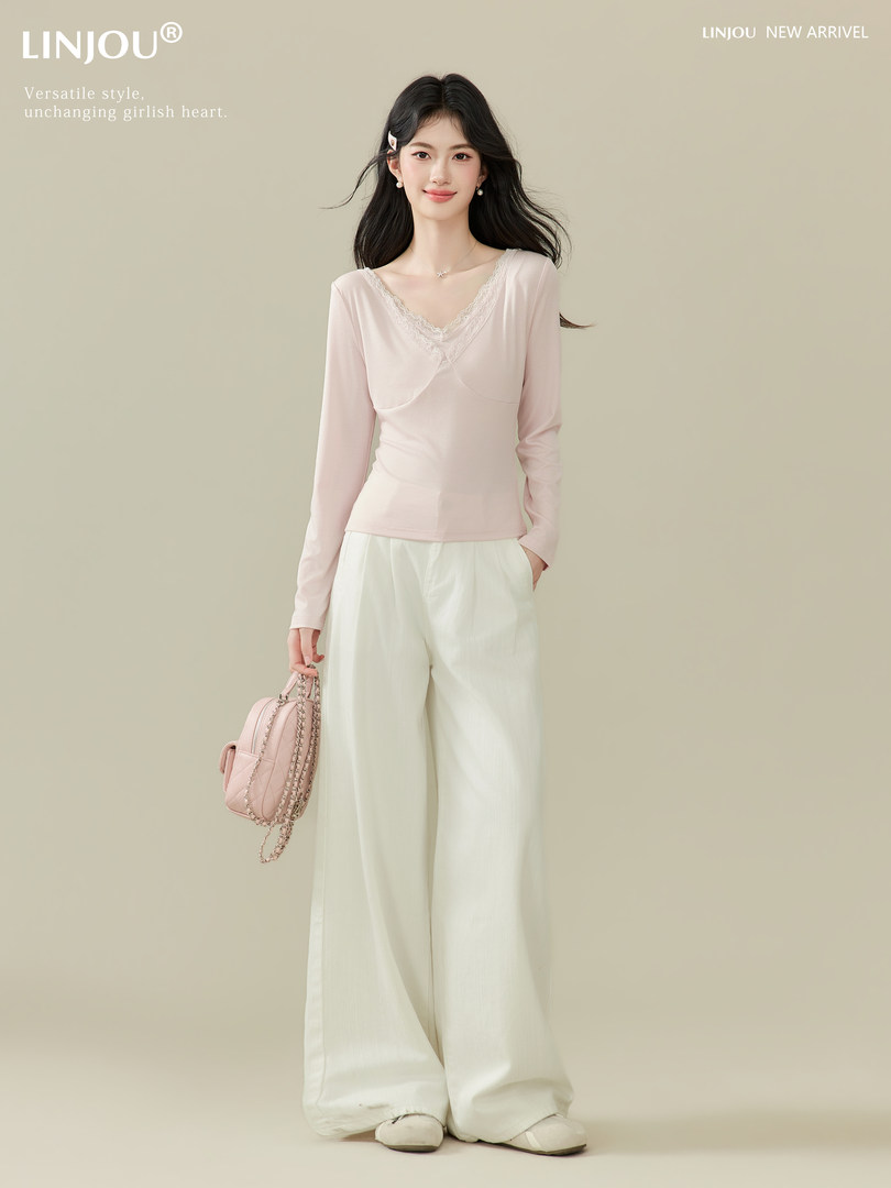 Model wearing a pale pink lace-trim long sleeve top with cream wide-leg pants and a pink handbag