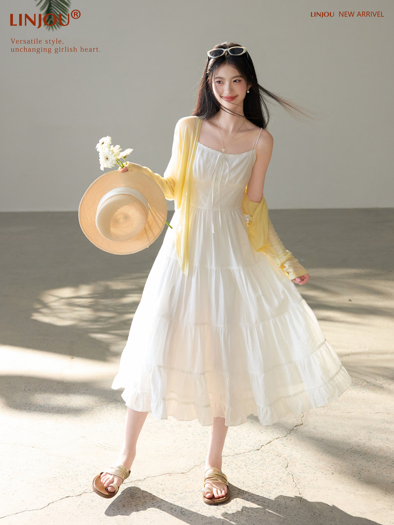 Woman wearing a white sleeveless summer dress with a yellow cardigan, holding a straw hat and flowers