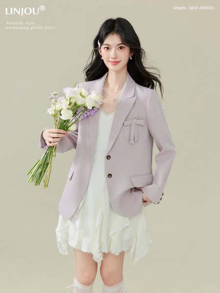 Model wearing a light lavender blazer over a white dress, holding flowers