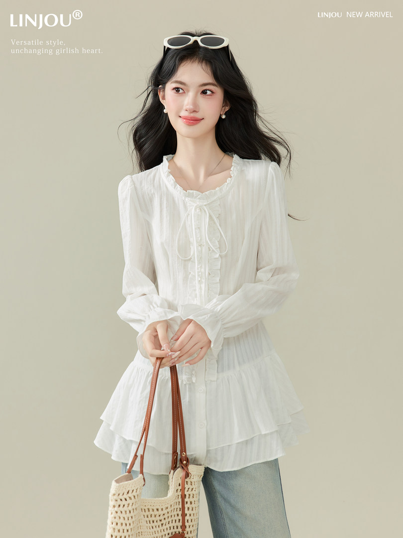 Model wearing a white ruffled long-sleeve blouse with jeans and a woven tote bag