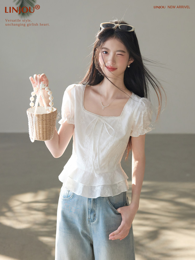 White lace short-sleeve blouse worn with light blue jeans and a small woven bucket bag