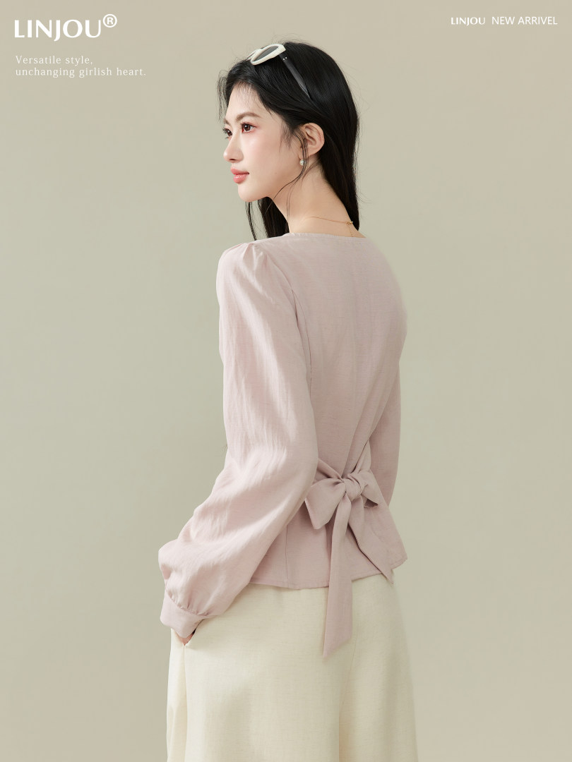 Model wearing a light pink long-sleeve wrap blouse with a back bow tie