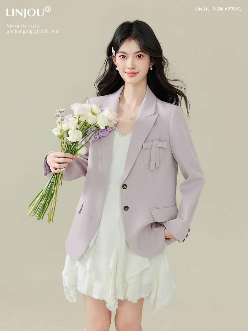 Model wearing a light lavender blazer over a white dress while holding a bouquet of flowers