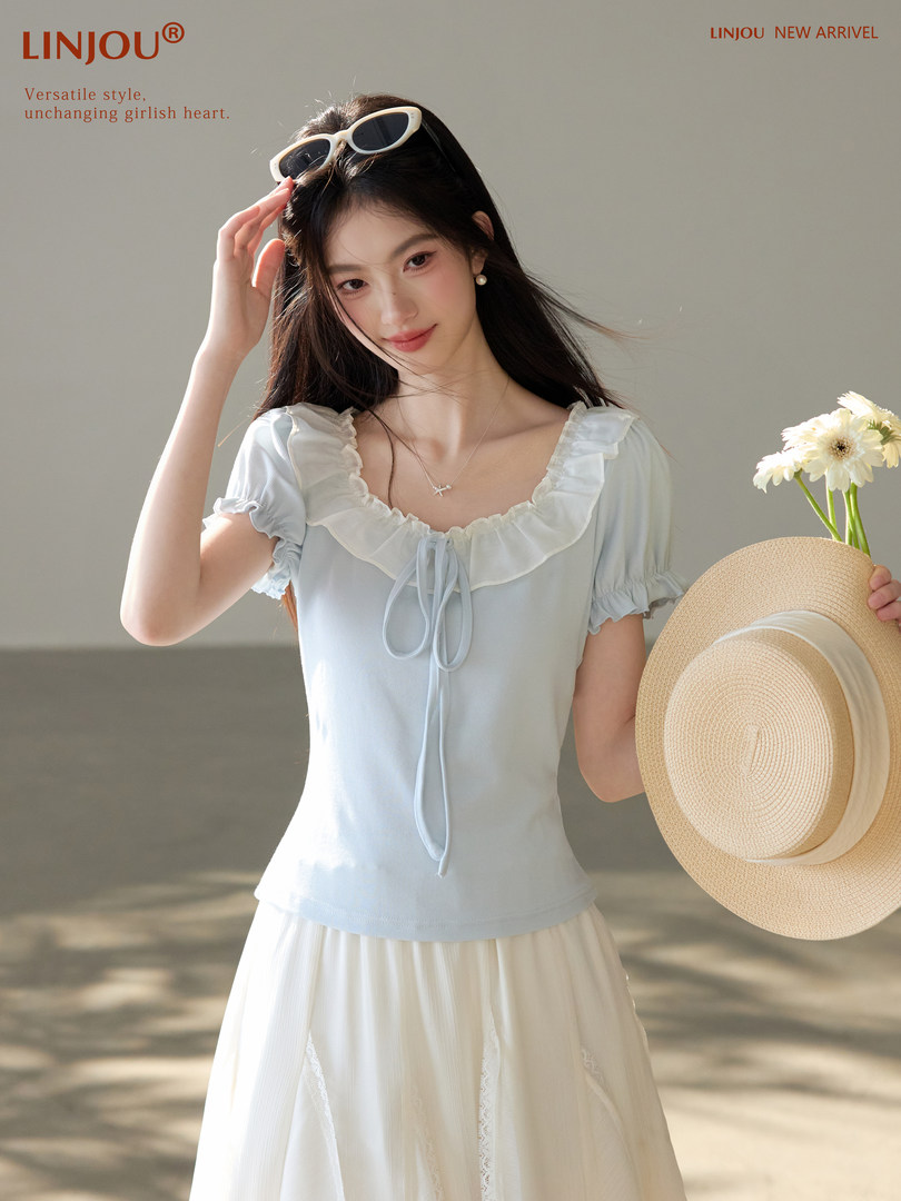Model wearing a light blue ruffled short-sleeve top with a cream skirt and straw hat