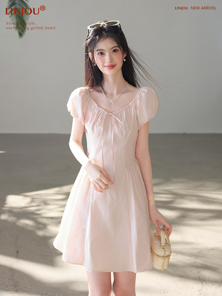 Model wearing a light pink short dress with puff sleeves and a small handbag