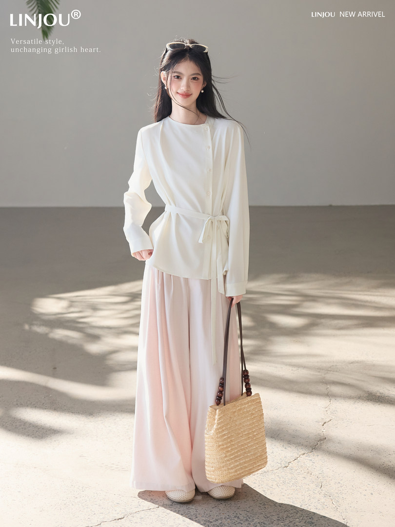 Model wearing a cream belted blouse with a pale pink wide-leg skirt and woven tote bag