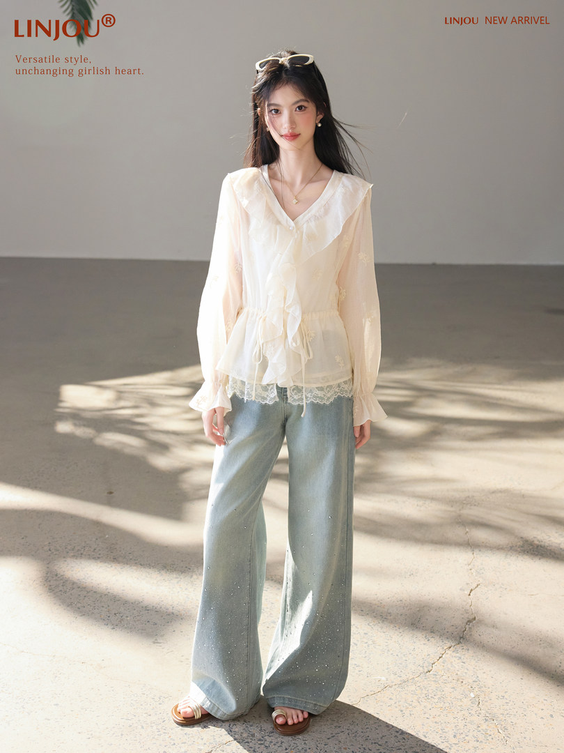 Model wearing a sheer cream blouse with light blue wide-leg jeans