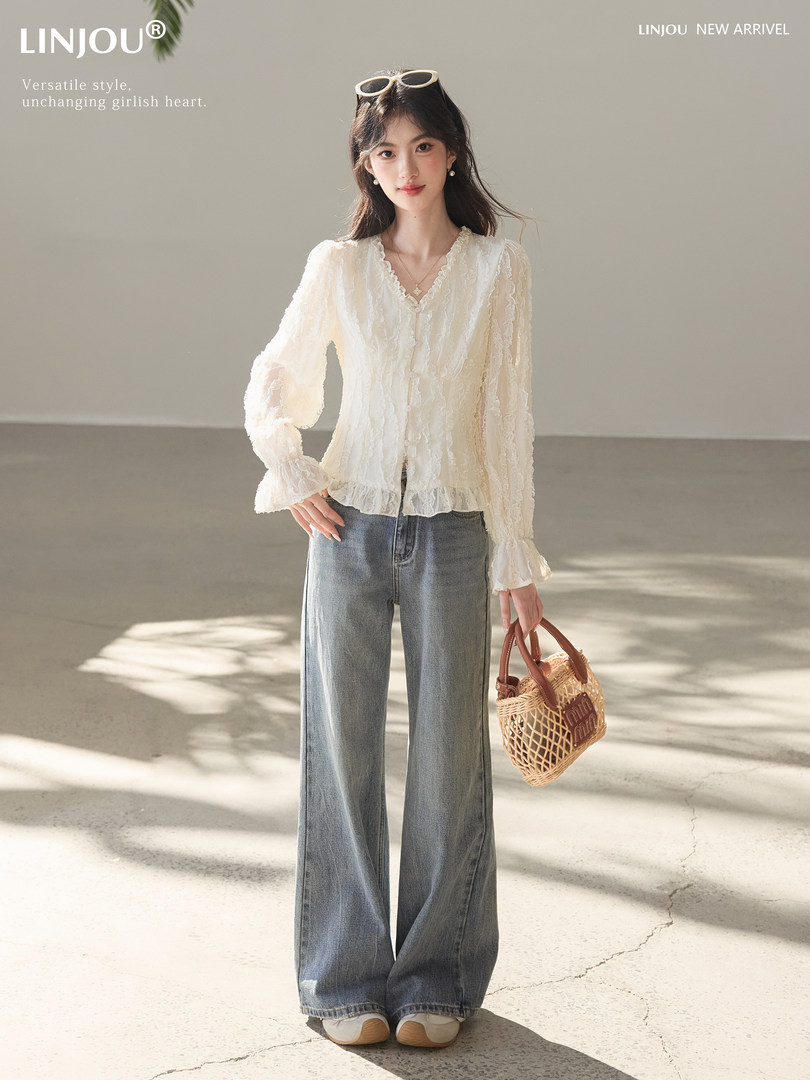 Model wearing a white ruffled blouse and wide-leg jeans, holding a woven handbag