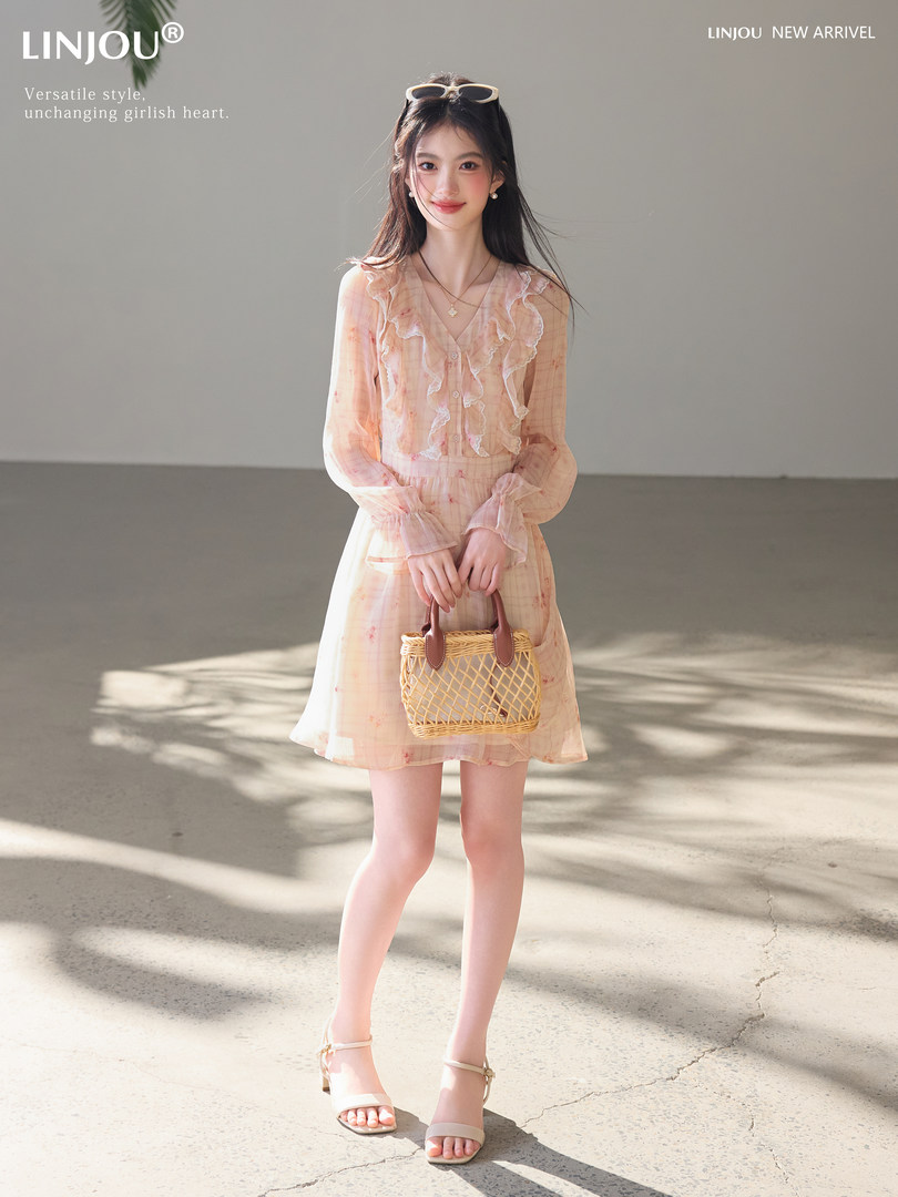 Woman modeling a light peach ruffled dress with a small woven handbag