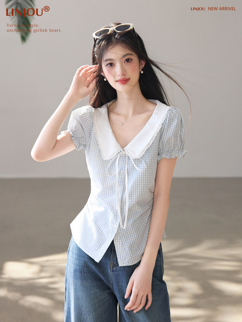 Model wearing a light blue checkered short-sleeve blouse with a large white collar and jeans