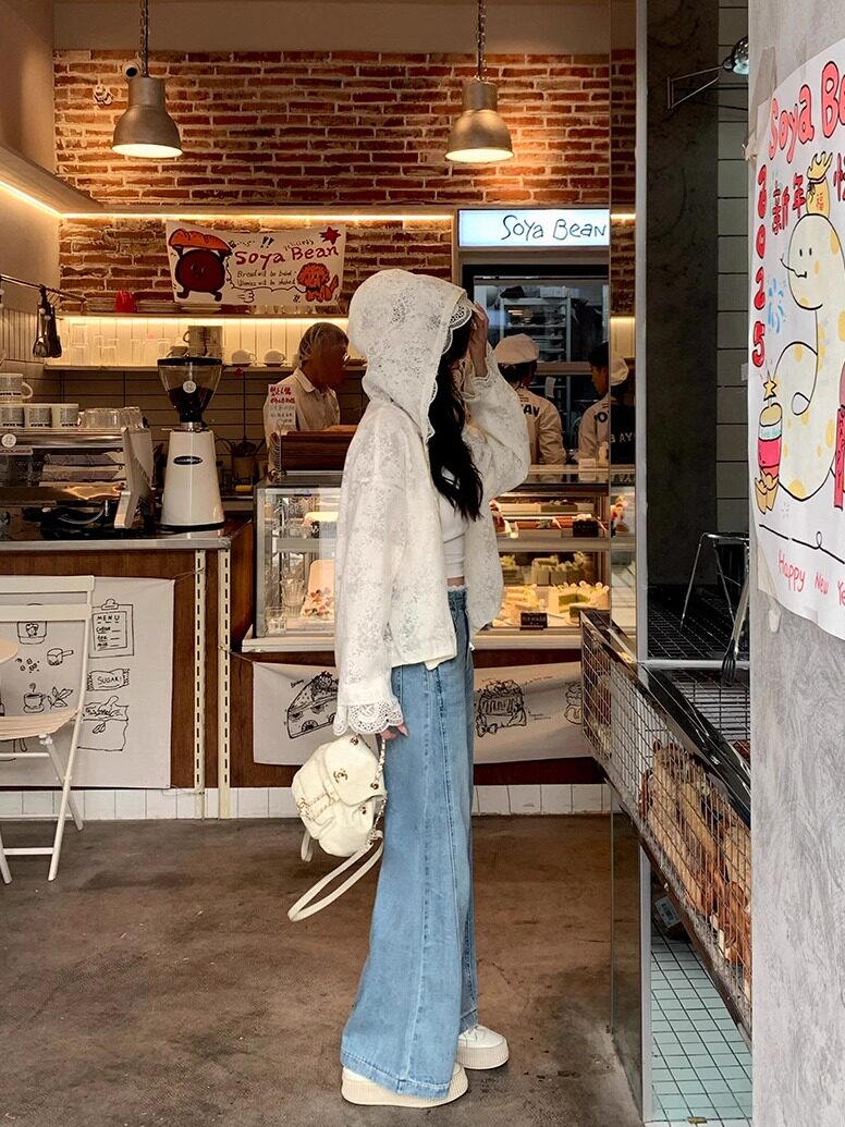Model wearing a white lace hooded jacket with wide-leg blue jeans and a small white backpack