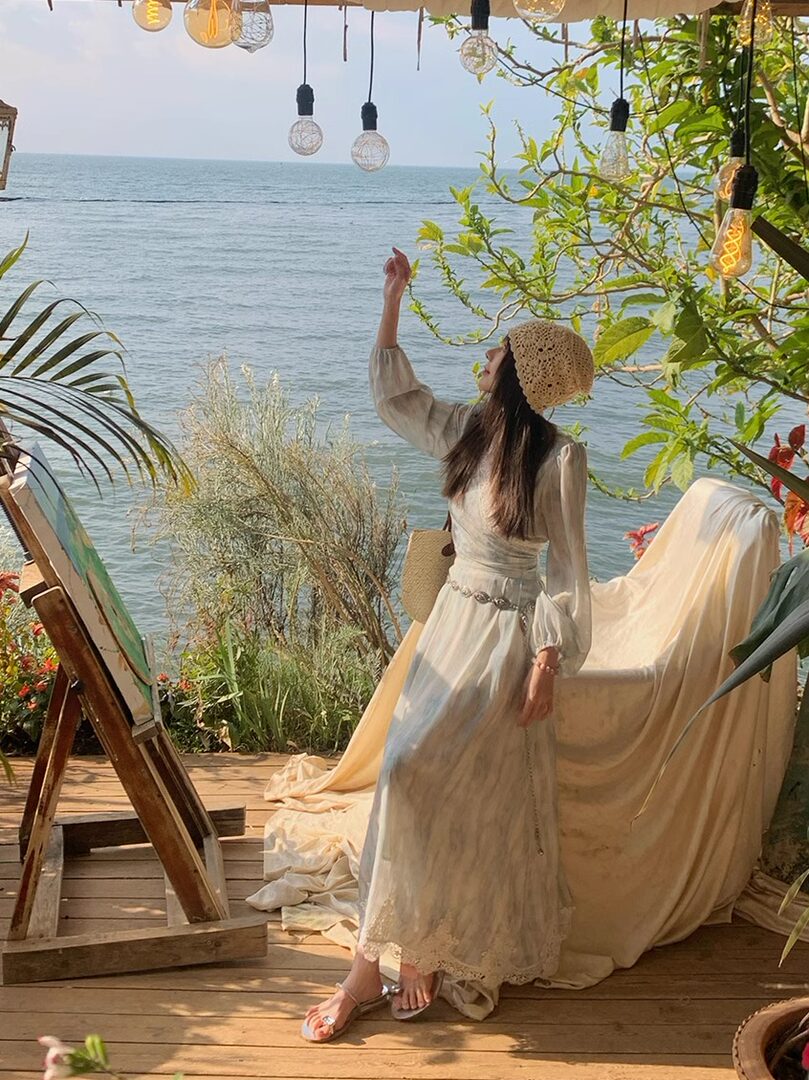 Woman wearing a light beige long dress and crochet hat by the seaside