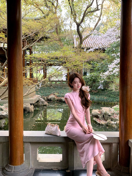 Woman wearing a pink fitted dress seated in a garden pavilion