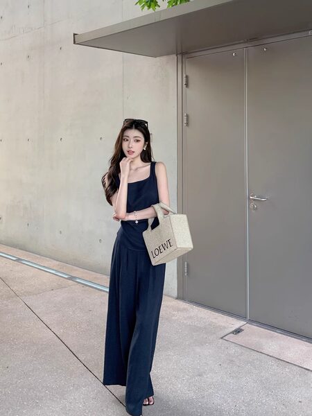 Woman wearing a navy sleeveless wide-leg outfit and carrying a woven Loewe tote bag