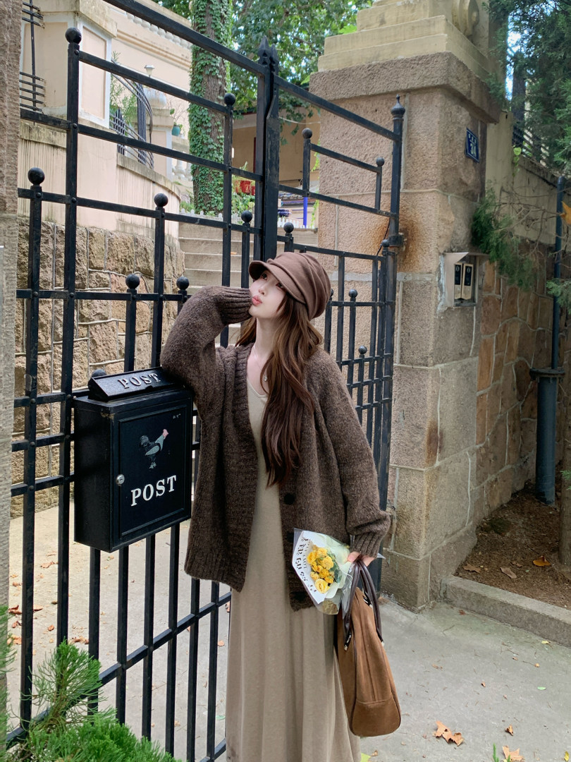 Woman wearing a brown knit cardigan and long dress outdoors by a gate