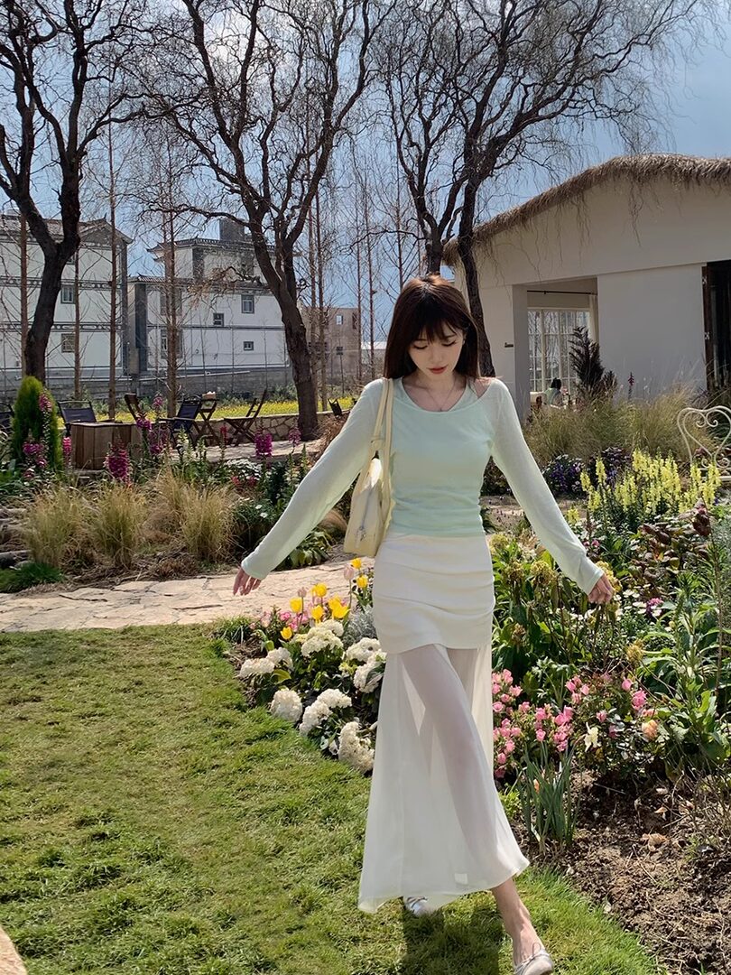 Woman wearing a light mint top and white sheer skirt in a garden setting
