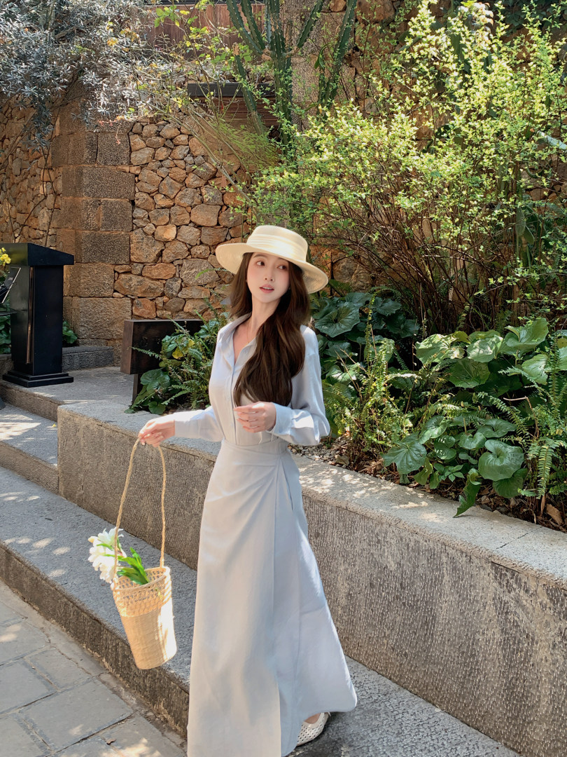 Woman wearing a light blue long dress and straw hat outdoors