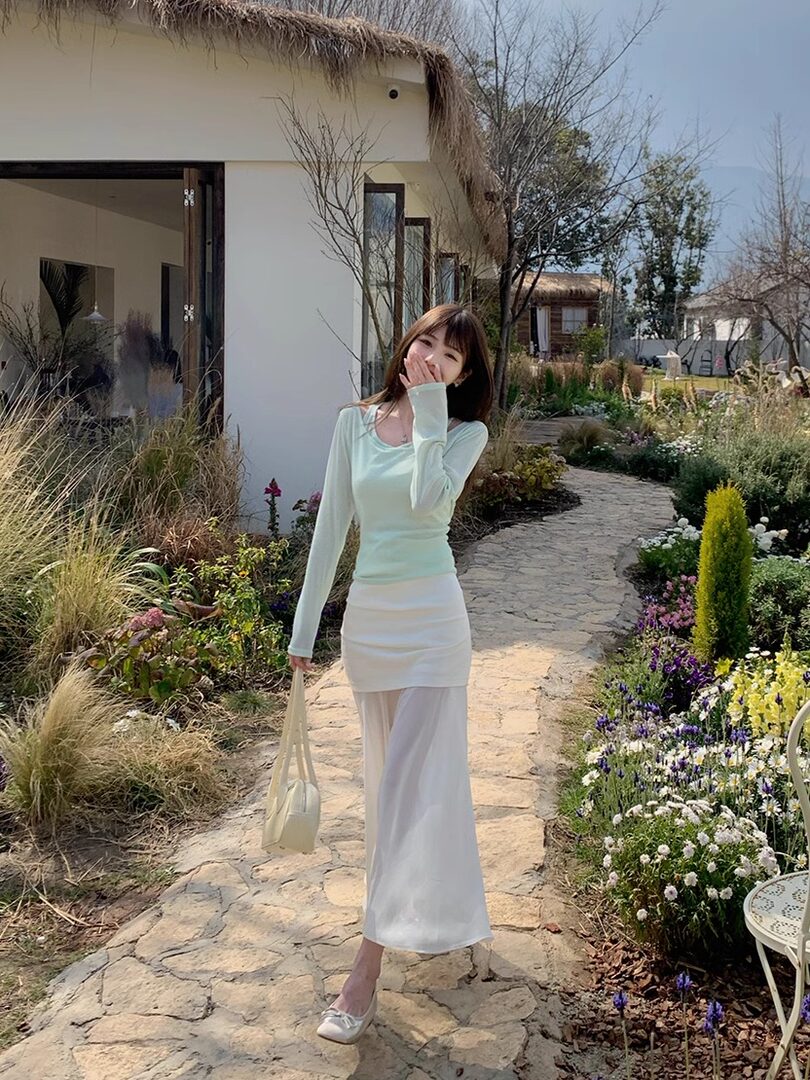 Woman wearing a light mint long-sleeve top with a white skirt and handbag outdoors