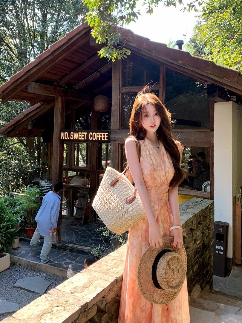 Woman wearing a peach sleeveless dress outdoors with a woven hat and straw bag
