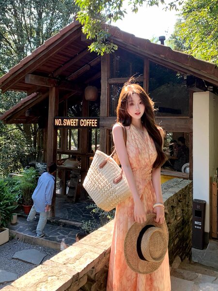 Woman wearing a peach sleeveless dress outdoors with a woven hat and straw bag