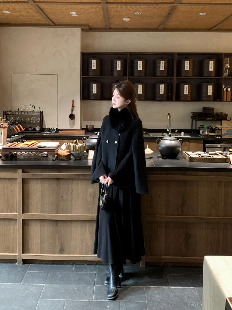 Woman wearing a black winter coat and long skirt indoors