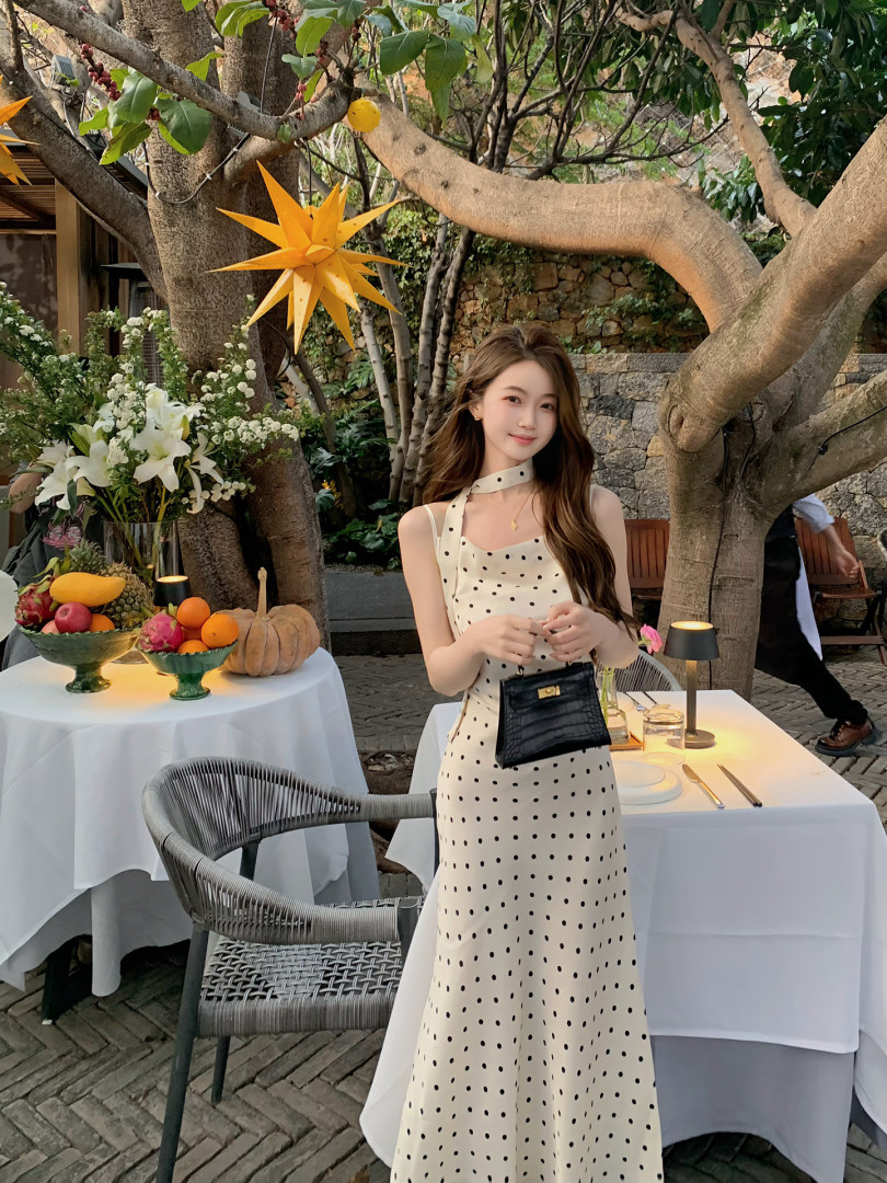 Woman wearing a cream polka dot halter dress and holding a black handbag outdoors