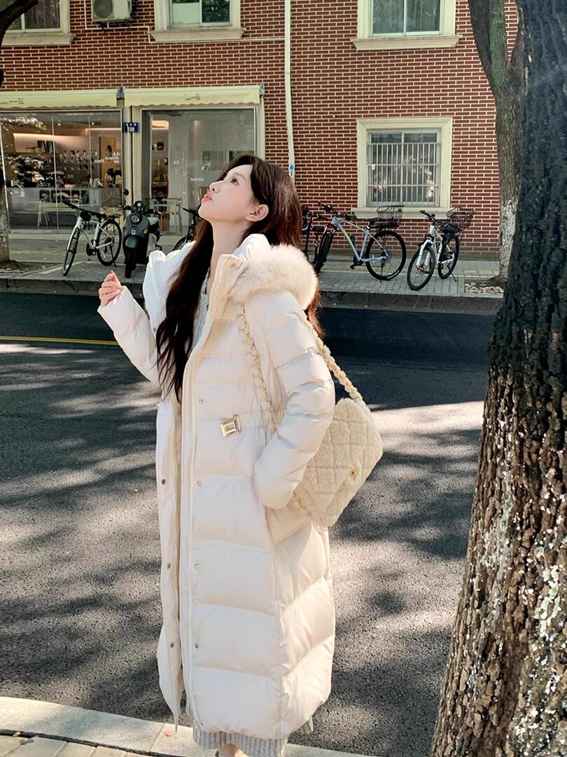 Woman wearing a cream puffer coat with fur-trim hood and quilted shoulder bag