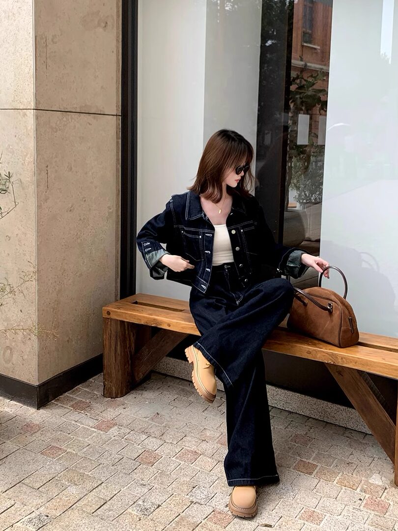 Model wearing a dark denim jacket and wide-leg jeans with beige boots and a brown handbag