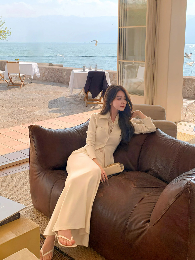 Woman wearing a cream elegant outfit seated on a sofa by the sea
