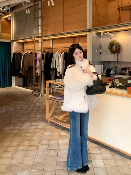 Woman wearing a white fur-trimmed coat with blue flared jeans and a black handbag in a boutique