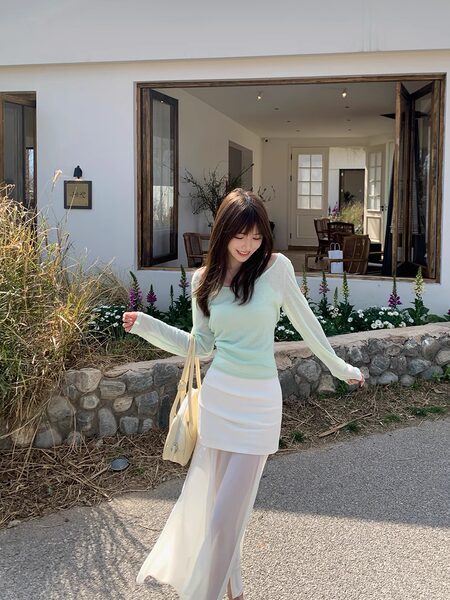 Woman wearing a light mint long-sleeve top with a white layered skirt and sheer overlay outdoors