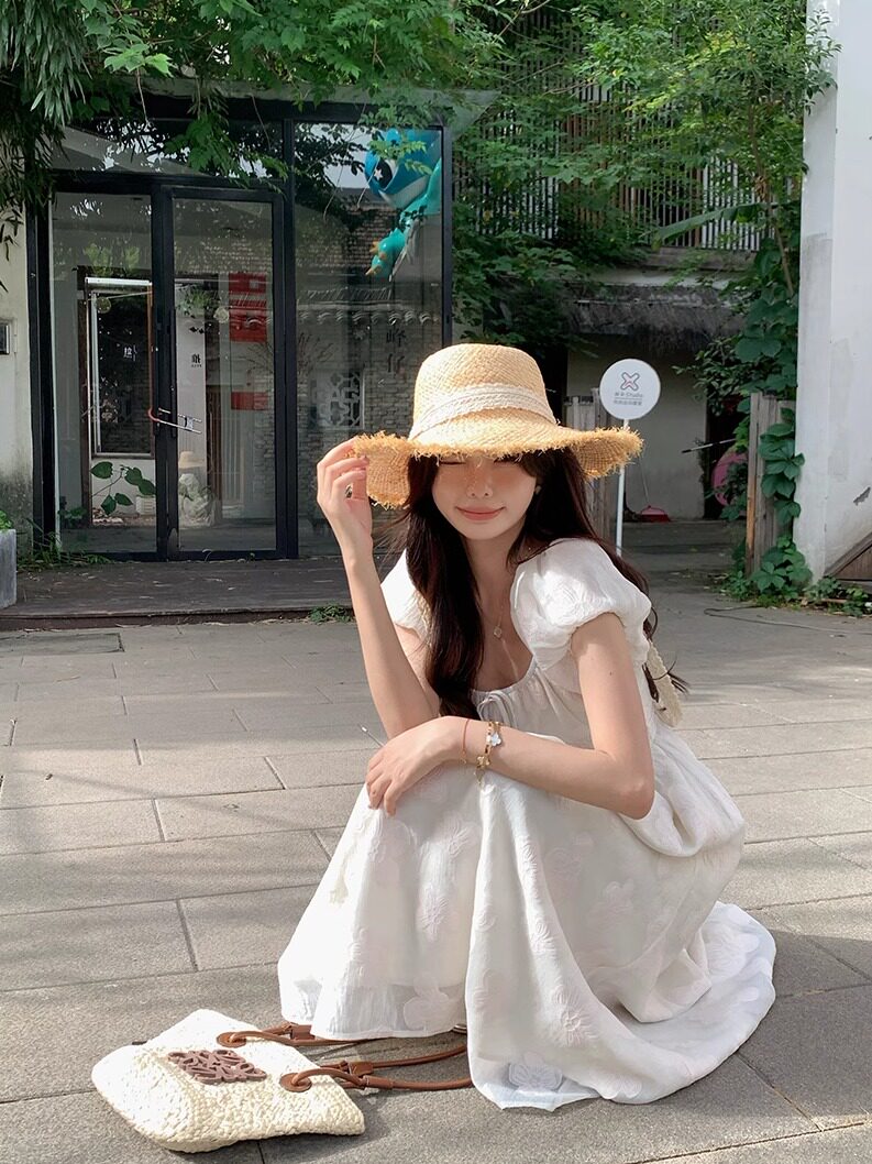 Woman wearing a white summer dress and straw hat outdoors