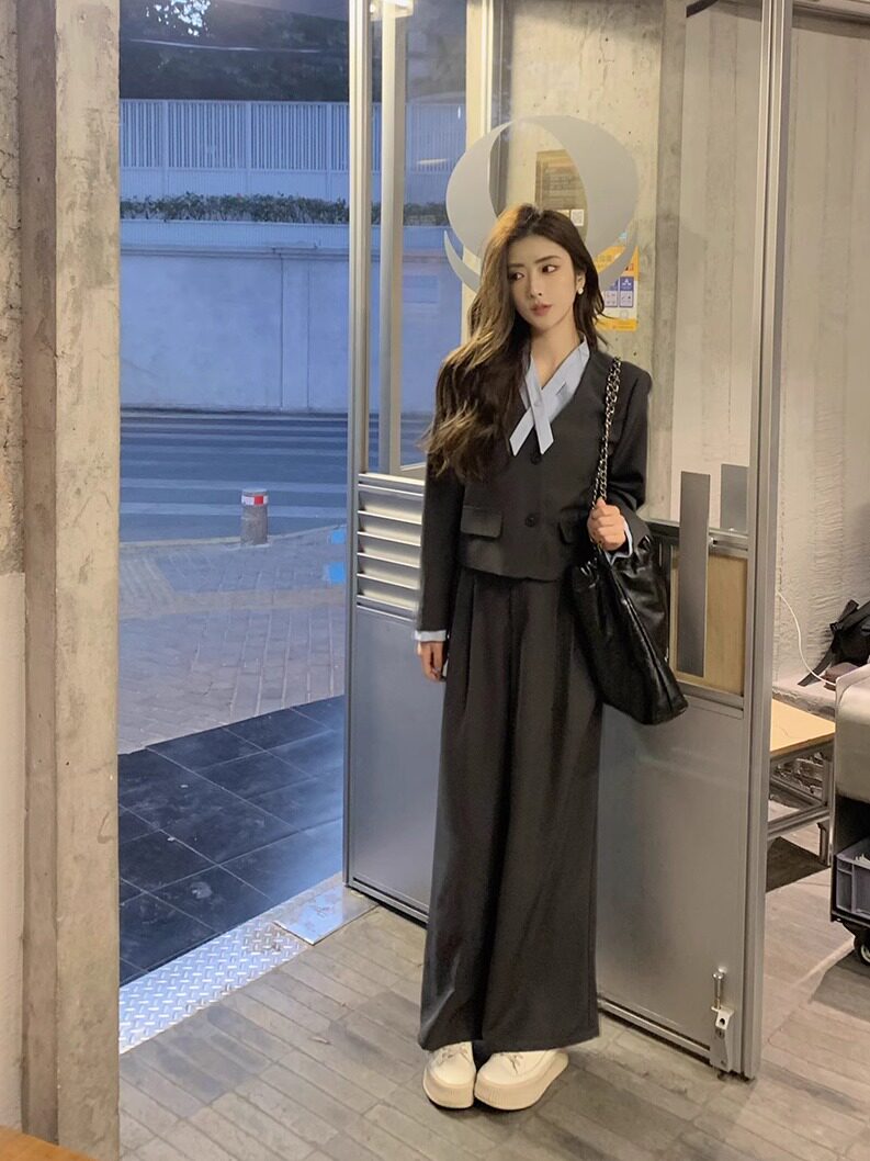 Woman wearing a black tailored blazer and wide-leg trousers with a light blouse and handbag