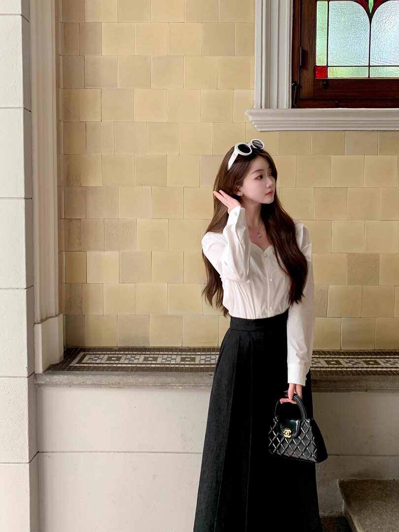 Woman wearing a white blouse with a black high-waisted long skirt and carrying a black handbag