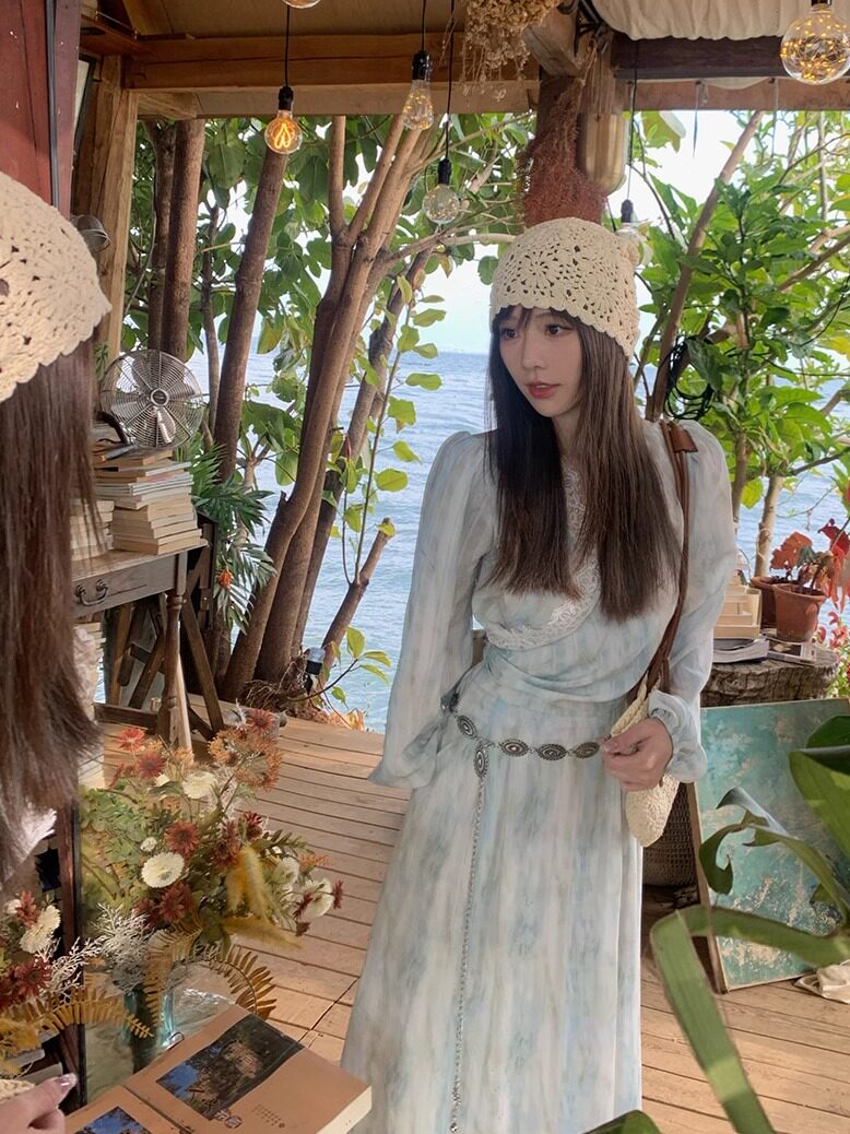 Woman wearing a light pastel dress and crocheted hat by the seaside