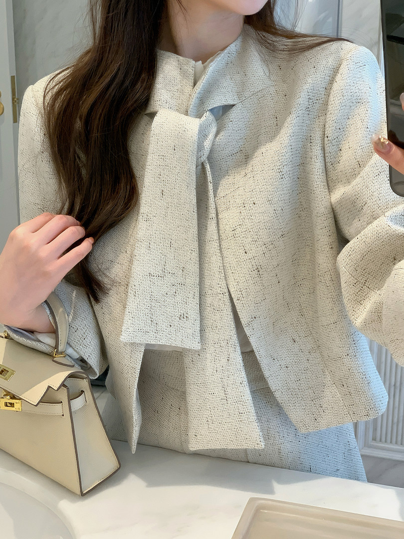 Woman wearing a light textured tweed jacket with a bow detail