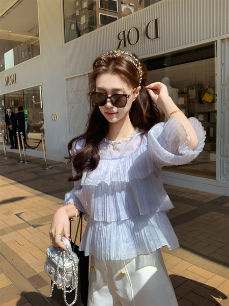 Woman wearing a light blue pleated dress outfit with sunglasses and a handbag