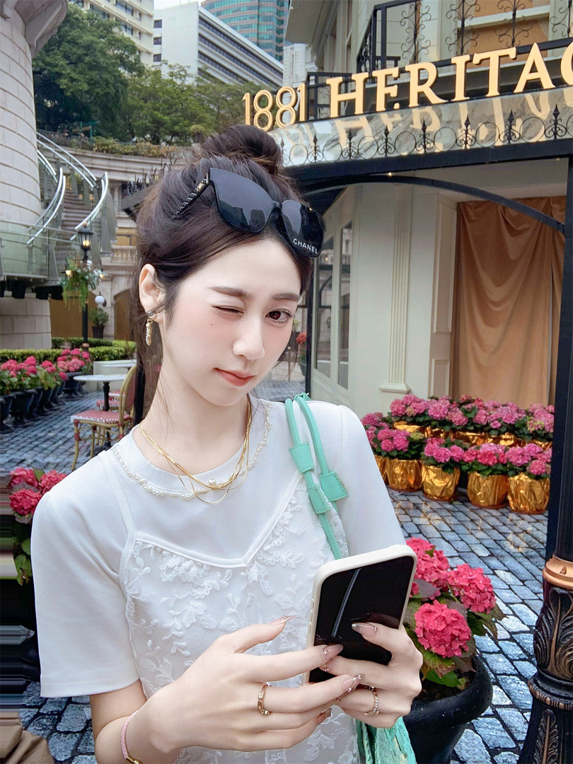 Woman wearing a white lace top and sunglasses, holding a phone outdoors