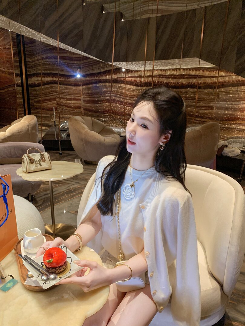 Woman wearing a light beige cardigan and white outfit in a café setting