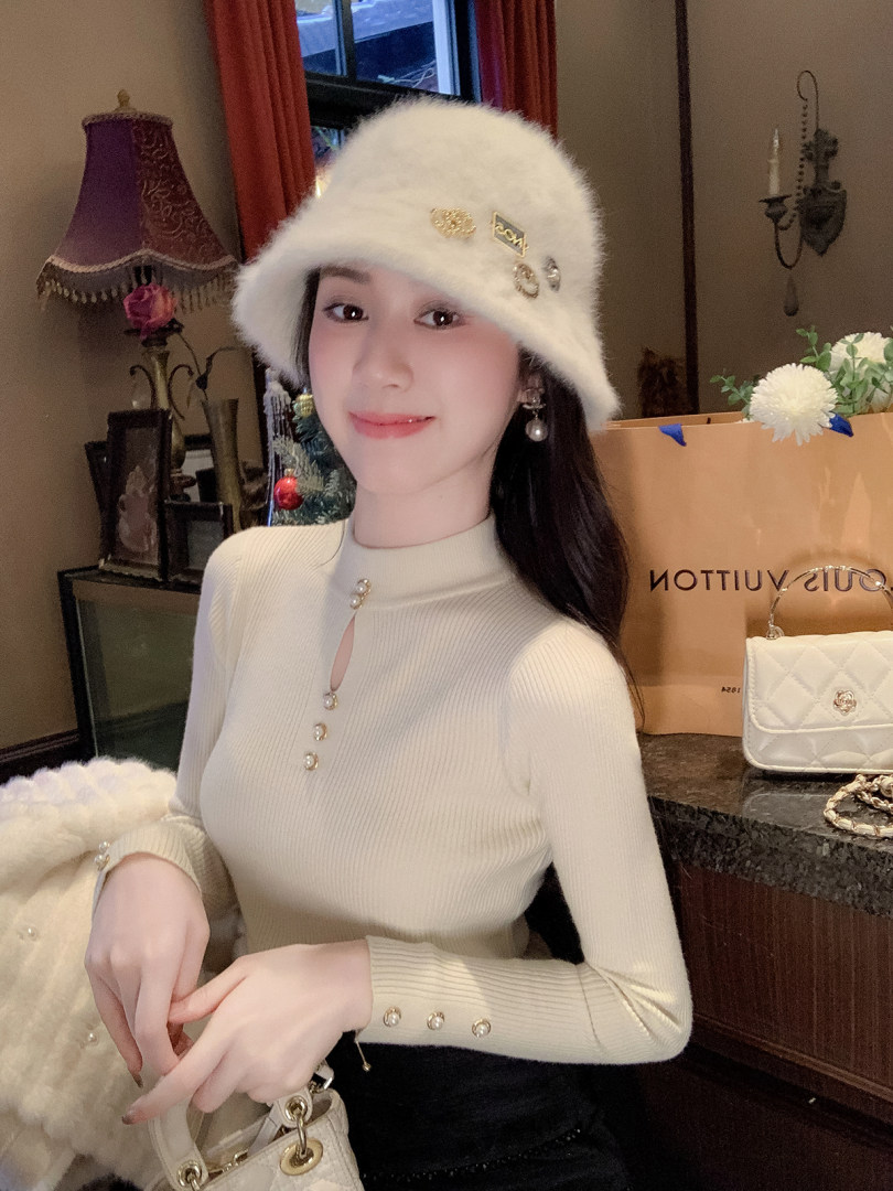 Woman wearing a cream ribbed top and fluffy white hat with a white handbag