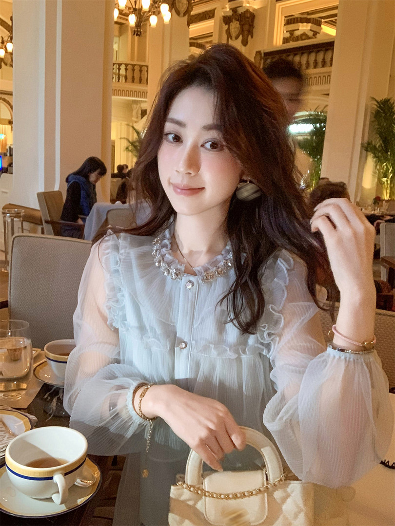 Woman wearing a sheer light blue ruffled blouse with a small cream handbag at a restaurant