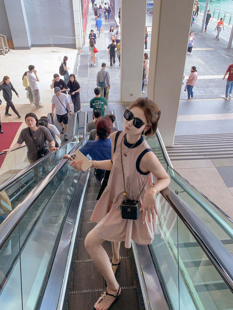 Woman wearing a sleeveless pink dress with sunglasses and a small crossbody bag on an escalator