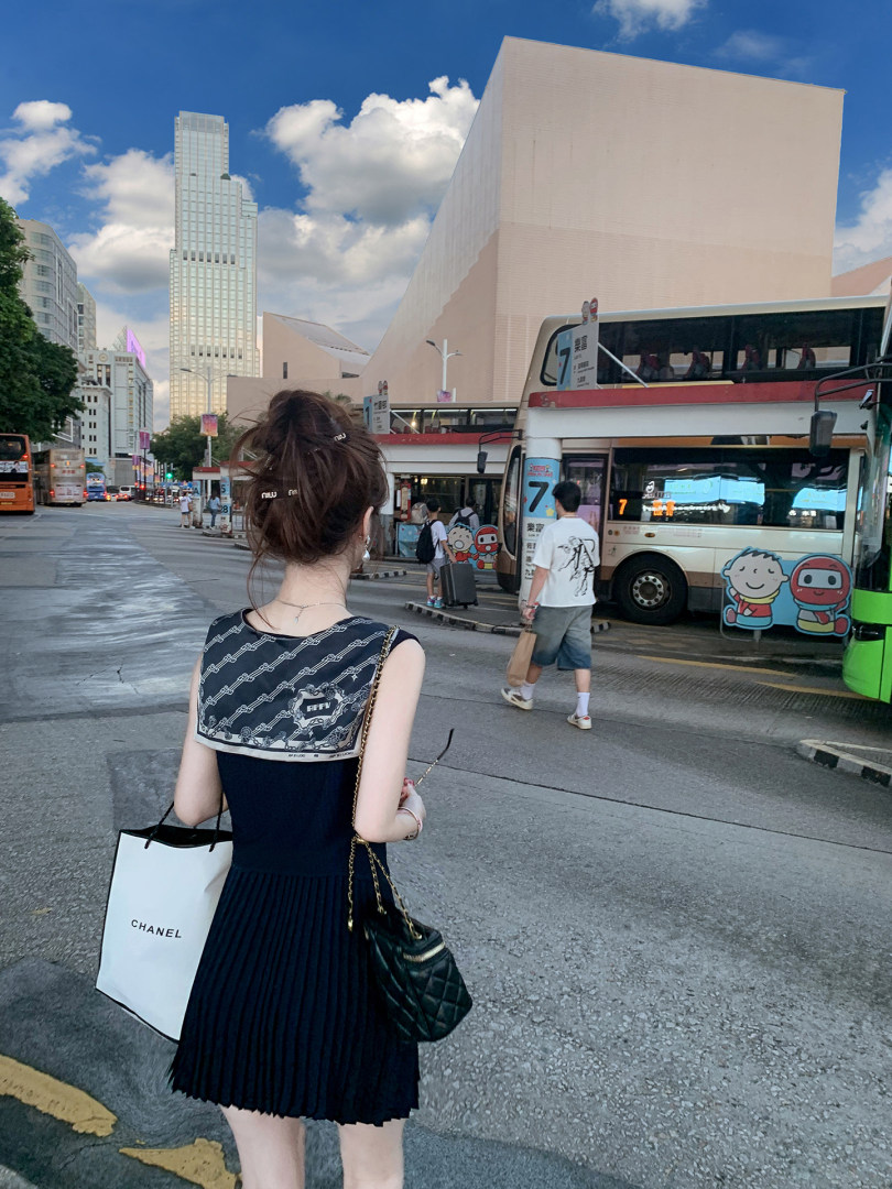 Woman wearing a black pleated sleeveless dress with a patterned scarf in a city street