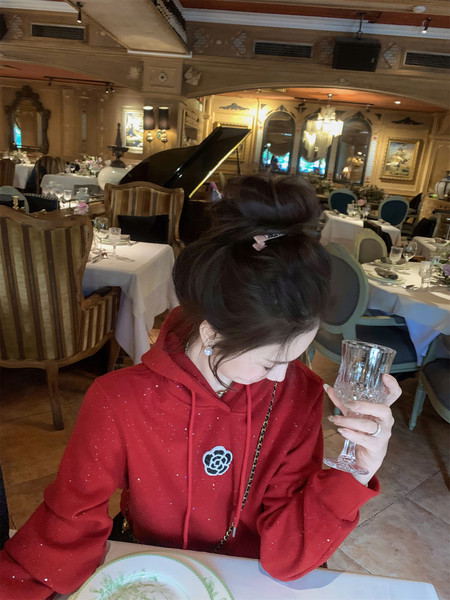 Woman wearing a red sparkly hoodie with a floral patch in a restaurant