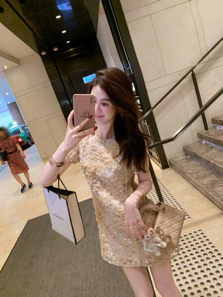 Woman wearing a beige lace dress and carrying a quilted handbag