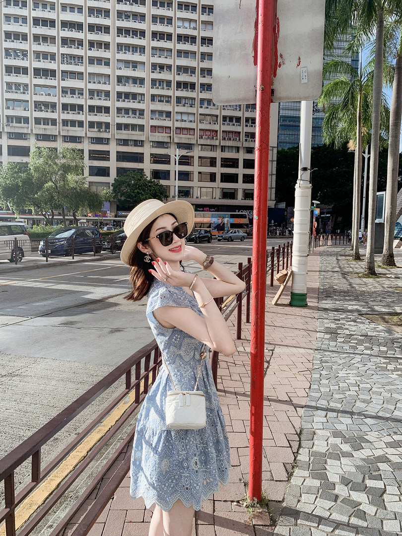 Woman wearing a light blue lace dress with a sun hat and crossbody bag outdoors