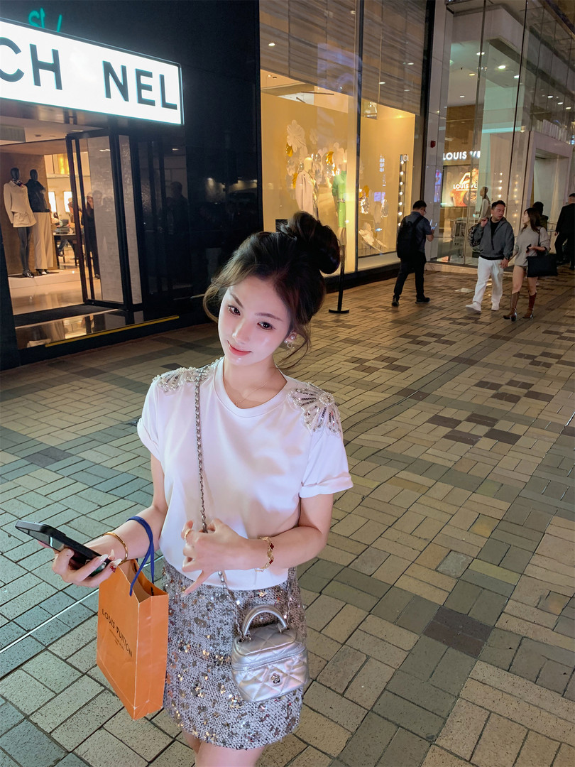 Woman wearing a white embellished T-shirt and a sequined mini skirt with a small silver handbag
