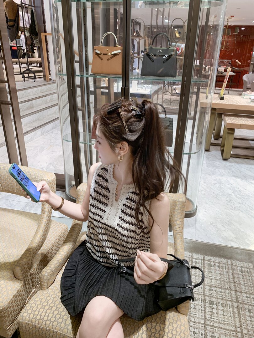 Woman wearing a striped sleeveless knit top with a black pleated skirt and carrying a black handbag