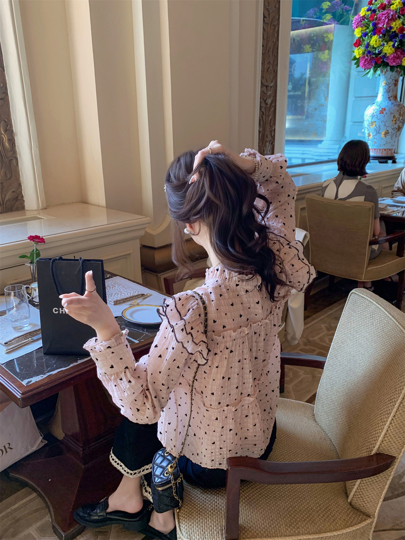 Woman wearing a pink heart-print ruffled blouse seated at a restaurant table